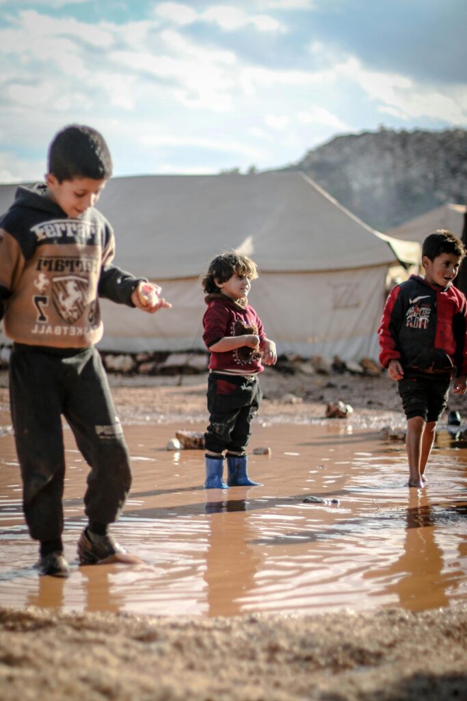 Refugee Children enjoying playtime in a muddy puddle at a refugee camp in Idlib, Syria.